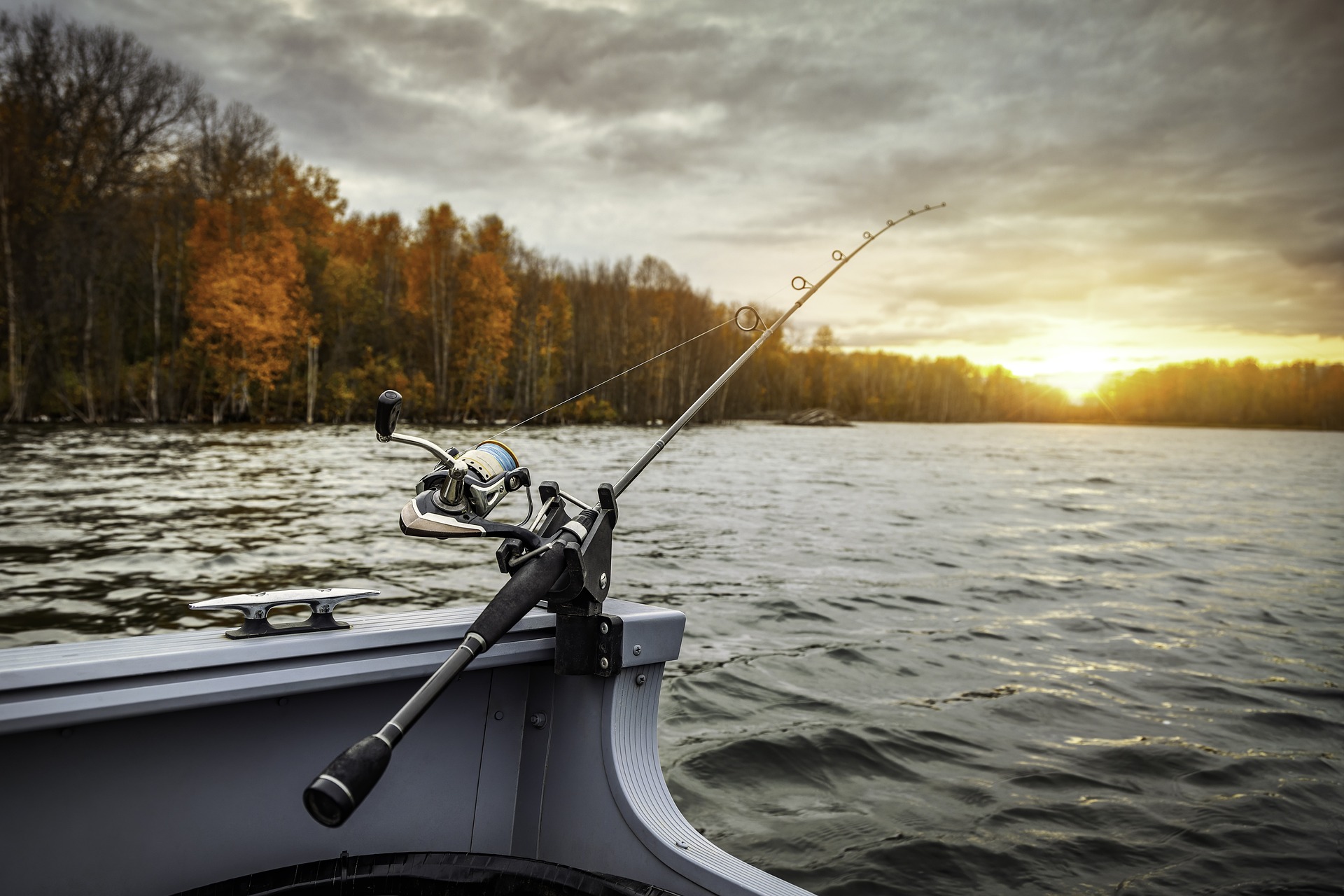 A fishing rod extends off a boat and over the river toward the sunrise on the horizon